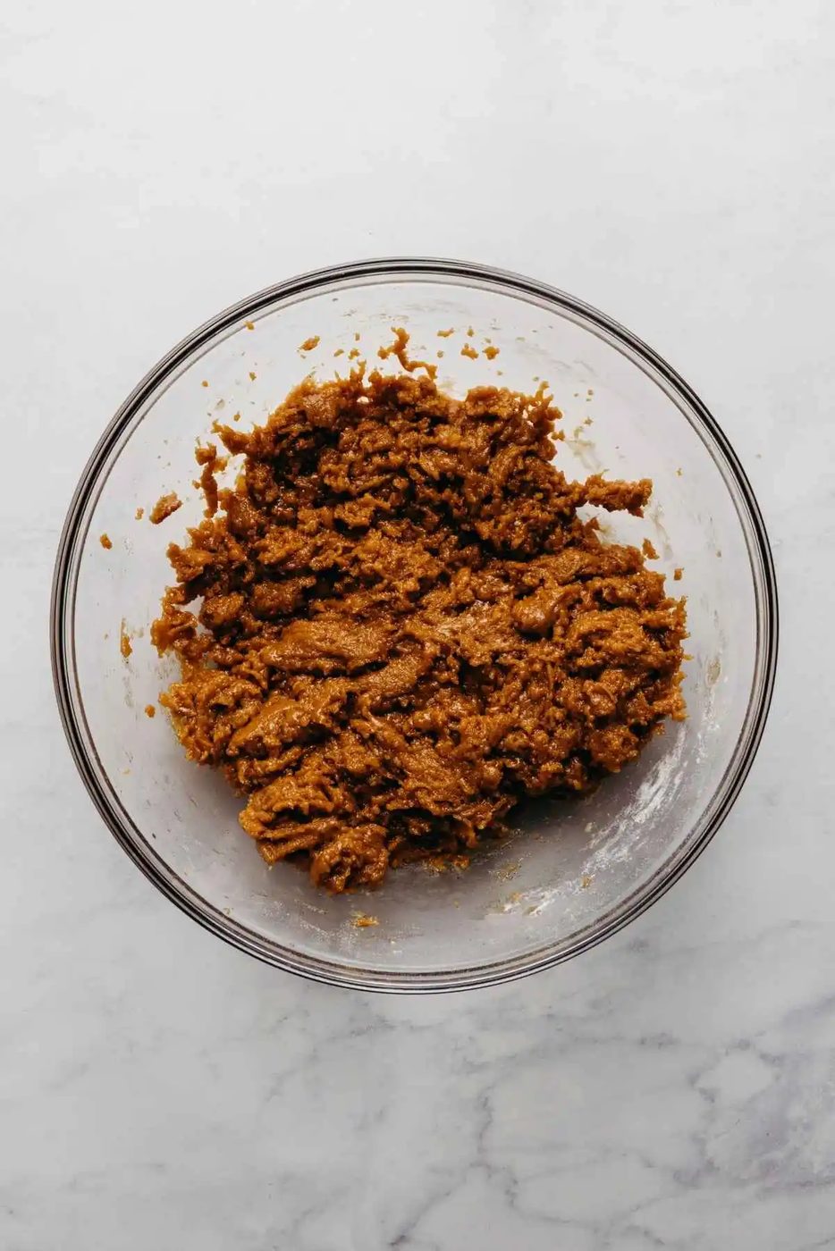 Molasses cookie dough in a glass mixing bowl on a white and grey marbled background.