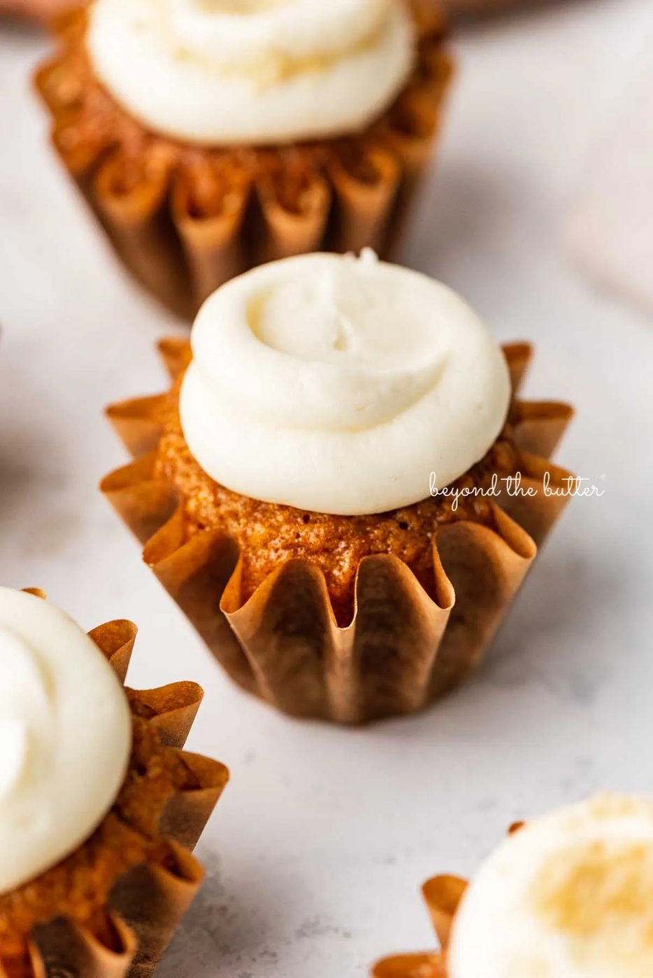 Carrot cake cupcakes topped with cream cheese frosting on a white background | © Sovuh