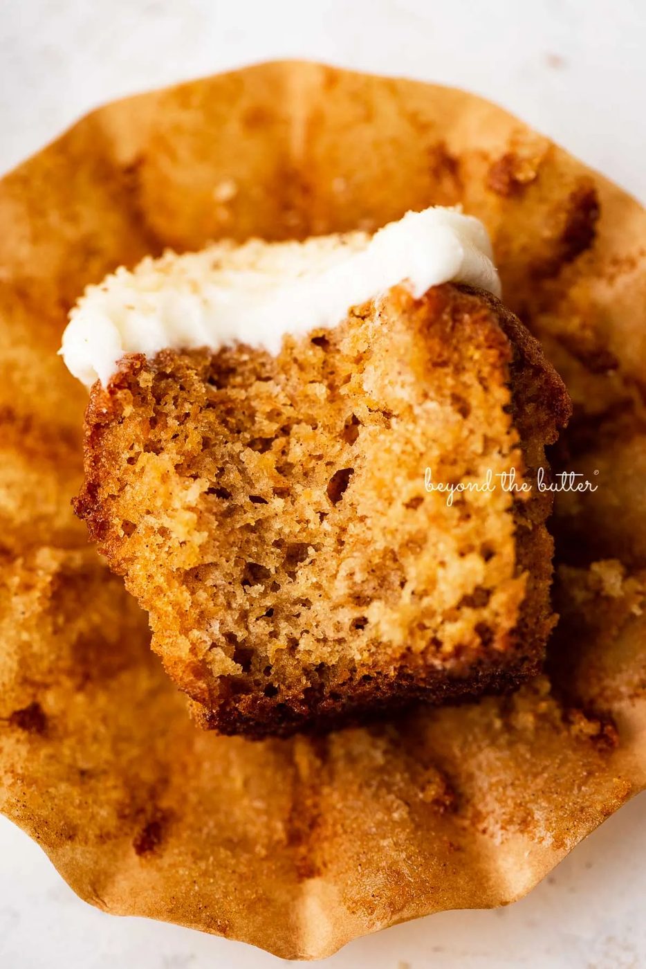 One unwrapped carrot cake cupcake with a bit taken out of it laying on its side.