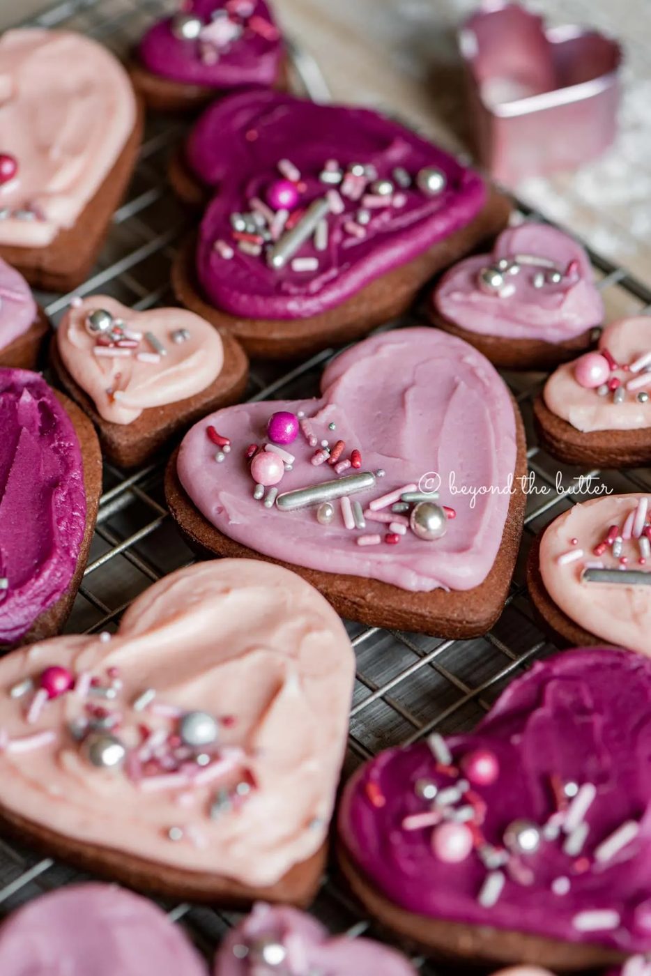 Angled image of decorated chocolate cut out sugar cookies on a wire cooling rack on light wood colored background | All Images © Sovuh
