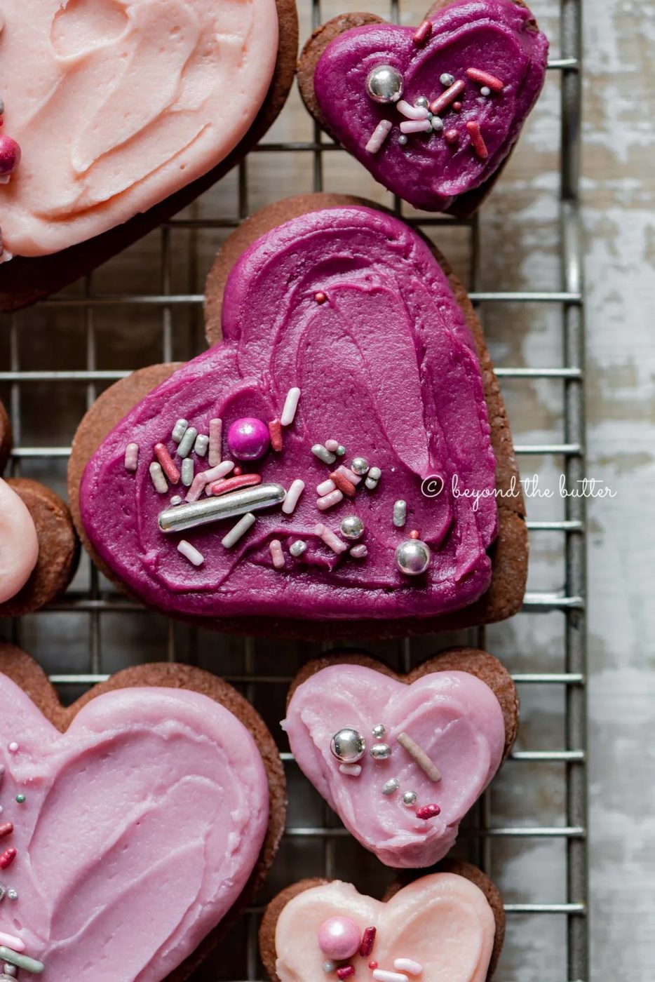 Closeup of decorated chocolate cut out sugar cookies on a wire cooling rack on light wood colored background | All Images © Sovuh