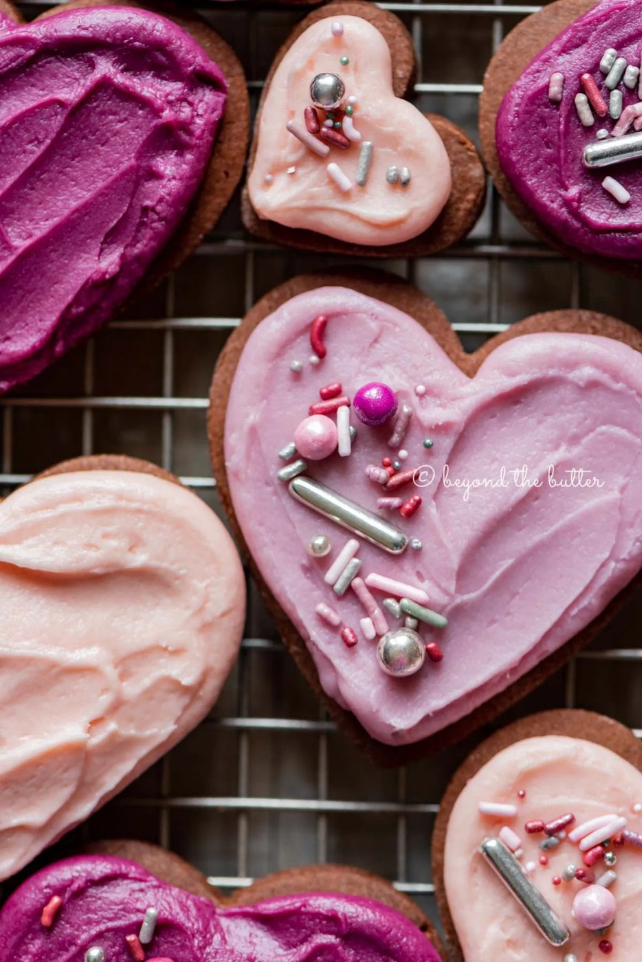 Closeup of decorated chocolate cut out sugar cookies on a wire cooling rack on light wood colored background | All Images © Sovuh