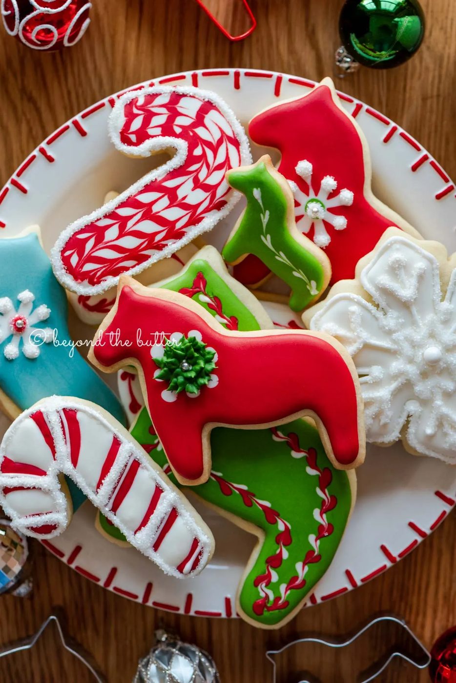 Plate of super soft cut out sugar cookies with royal icing with ornaments and cookie cutters around it | All Images © Sovuh