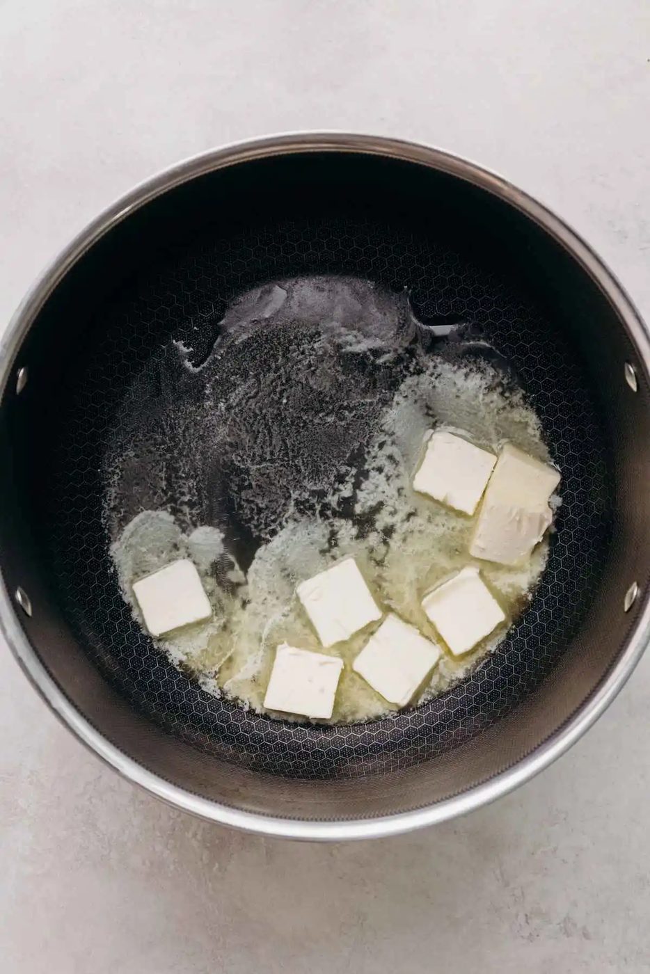 Melting butter in a large nonstick stock pot for rice krispie treats on a white and grey marbled background.