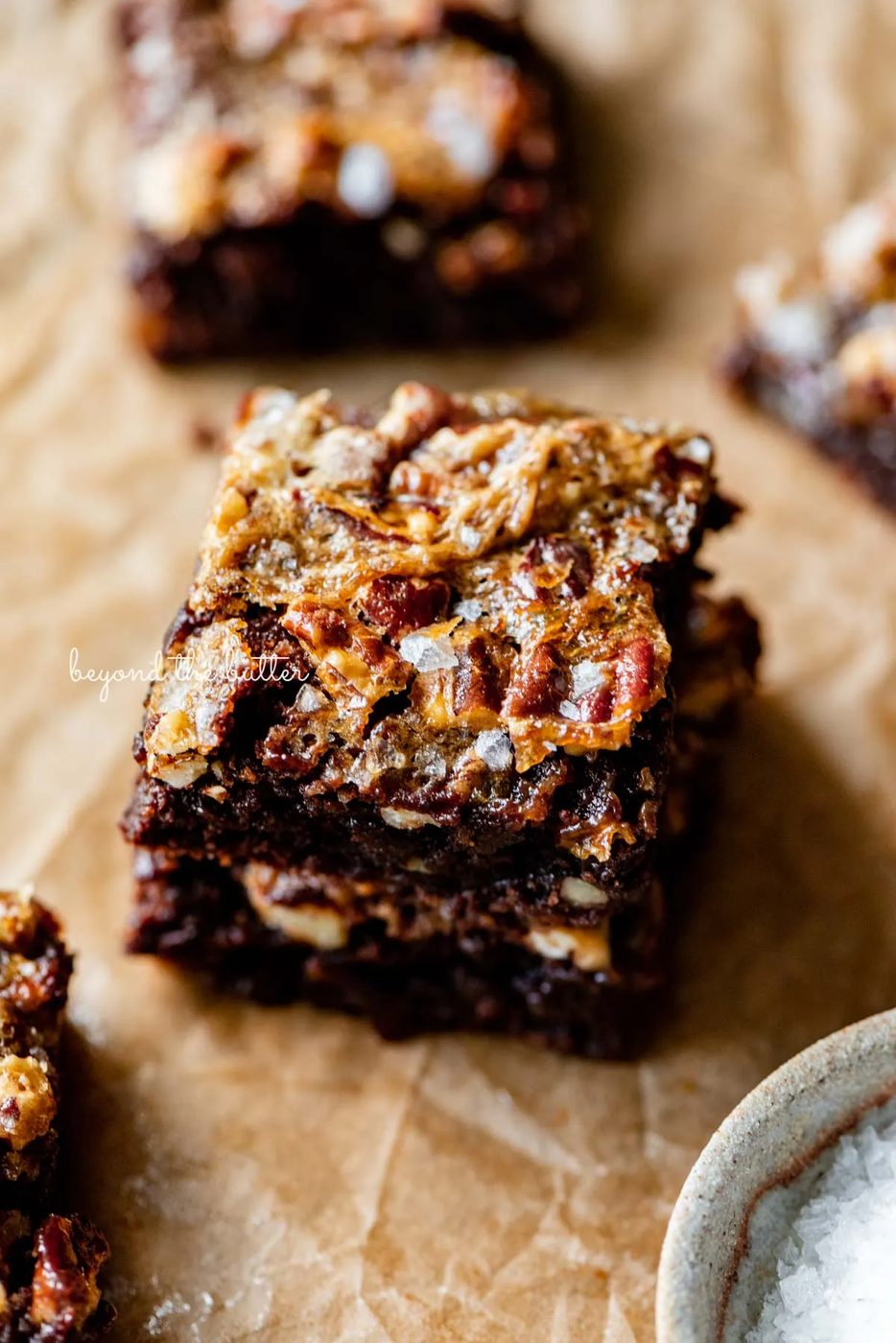 Stacked salted pecan pie brownies on brown parchment paper | © Sovuh