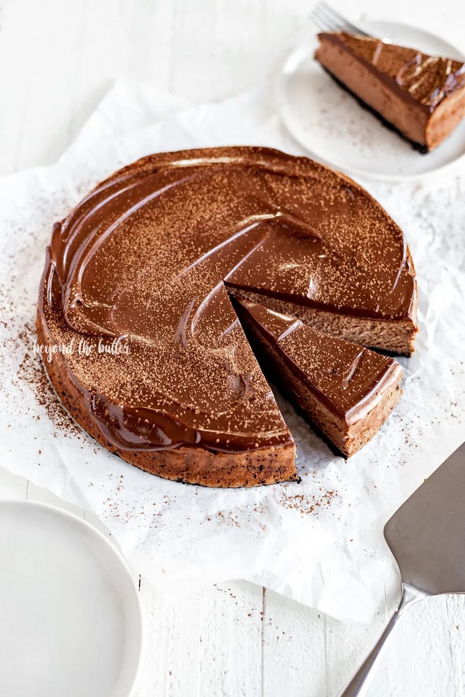 Overhead angled image of Triple Chocolate Mocha Cheesecake dusted with cocoa and a slice removed | All Images © Sovuh, LLC