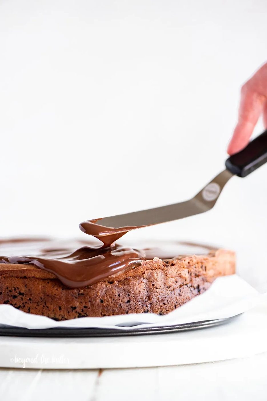 Using an offset spatula to spread out the dark chocolate ganache on top of the Triple Chocolate Mocha Cheesecake | All Images © Sovuh, LLC