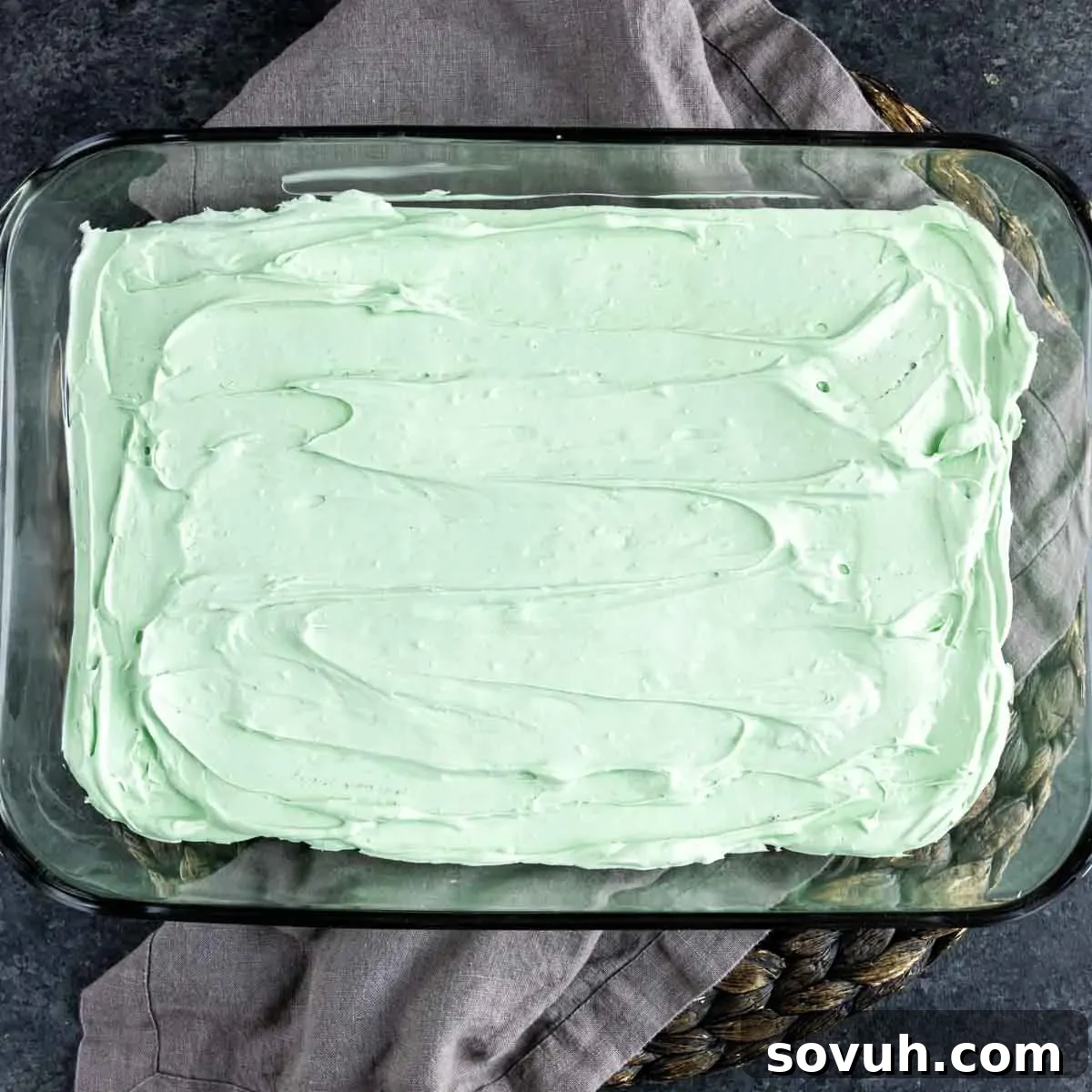 The vibrant green mint cream cheese layer smoothly spread over the Oreo cookie base in a clear glass baking dish.