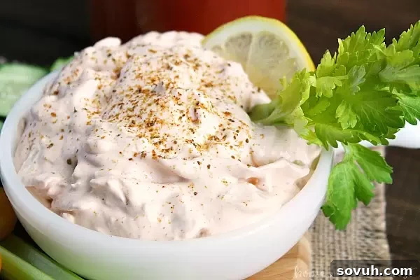A close-up shot of the creamy Bloody Mary Crab Dip in a bowl, showing its texture and enticing blend of colors, garnished with a celery stick.