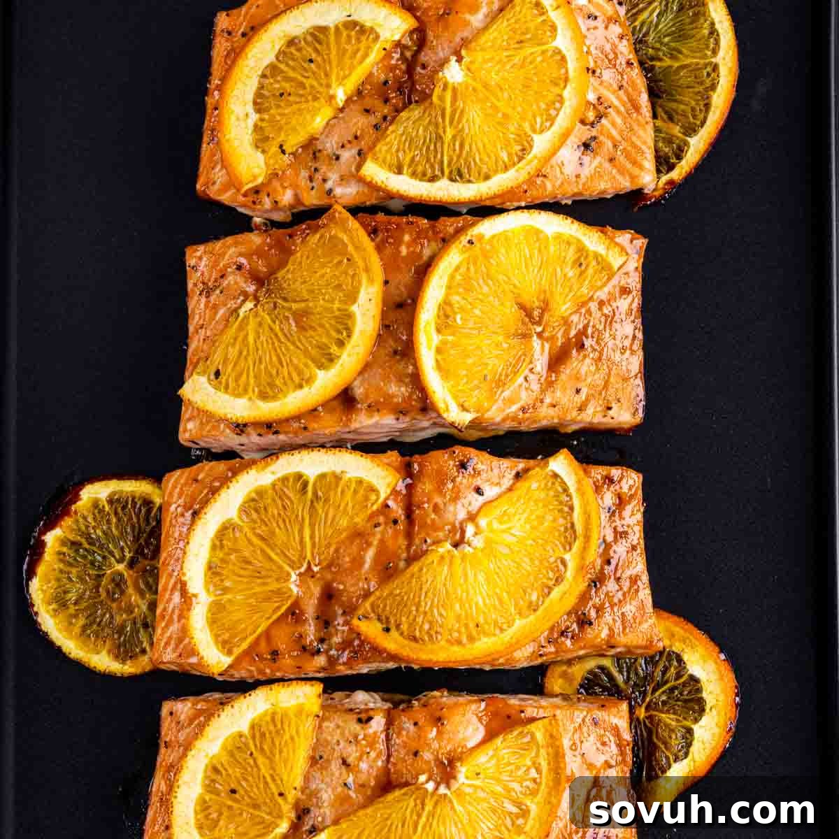 Citrus-Kissed Salmon 2 Four pieces of Orange Glazed Salmon topped with orange slices on a black surface.