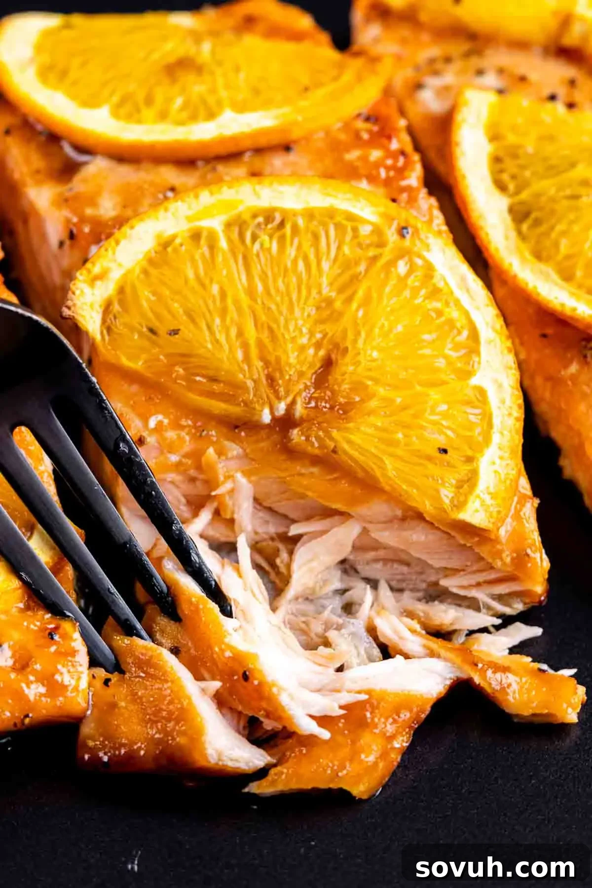 Citrus-Kissed Salmon 8 Orange Glazed Salmon fillets served with slices of orange on a black plate.