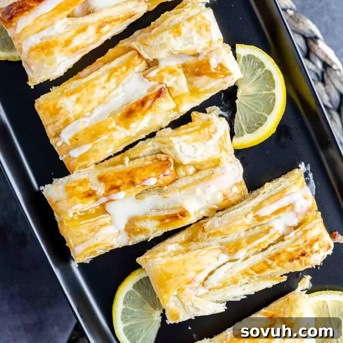 cut Lemon Cream Cheese Danish on black plate with fresh lemon slices