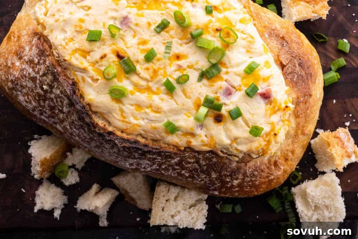 A loaf of bread filled with creamy dip, garnished with chopped green onions, surrounded by torn bread pieces.