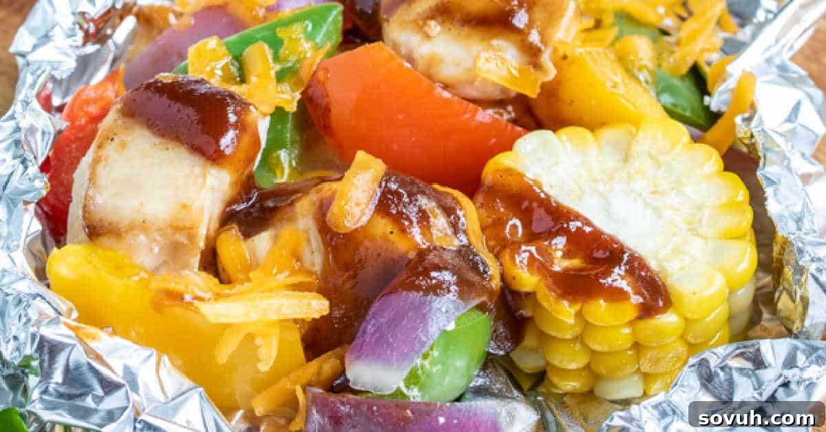 An assortment of grilled vegetables and chicken in a foil packet, including corn, red and green bell peppers, onions, and cheese, topped with sauce.