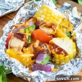 Grilled vegetables and chicken cubes with barbecue sauce in an aluminum foil package. Corn, bell peppers, and onions are visible.