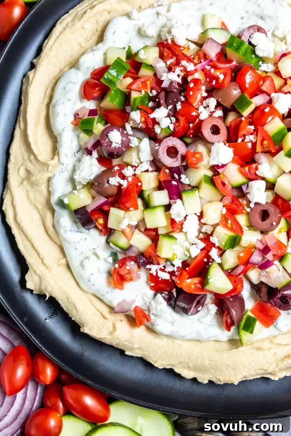5 Layer Greek Dip featuring fresh cucumber and tomato salad on top