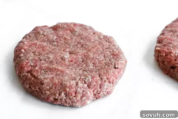 A raw burger patty made from seasoned ground beef, ready for grilling, demonstrating proper patty formation.