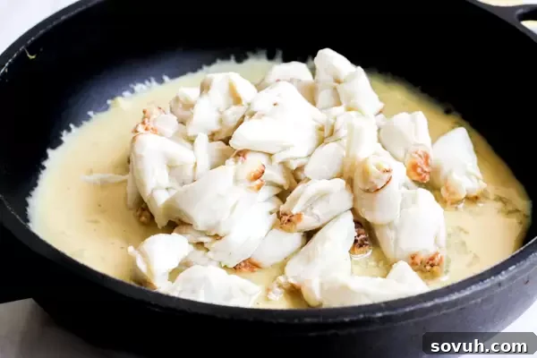 Lump crab meat being gently cooked in a flavorful sauce within a saucepan, ready to top the burger.