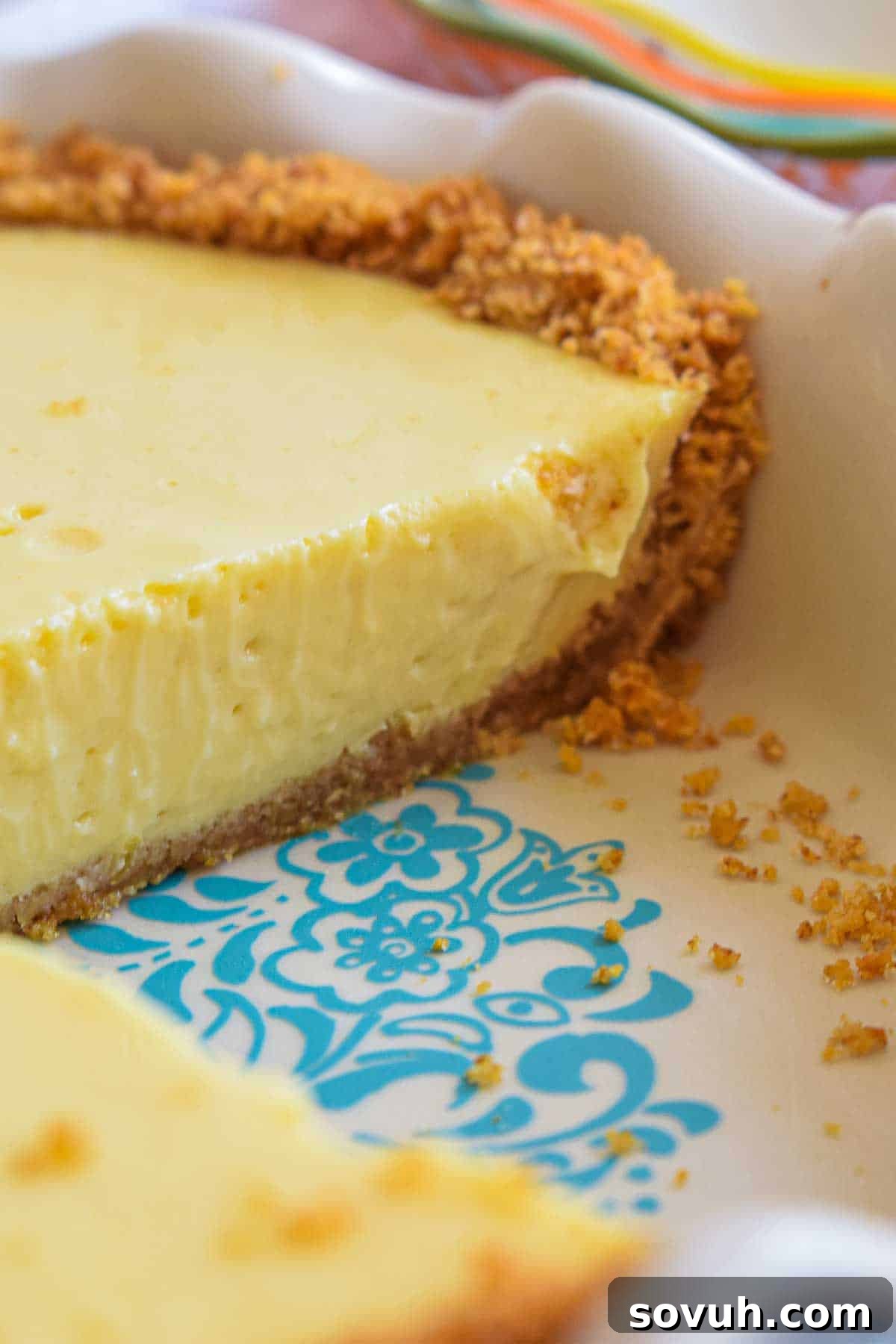 Zesty Lemon Icebox Pie 4 A whole Lemon Icebox Pie in a decorative ceramic pie dish with a teal pattern, showcasing its beautiful golden crust and smooth yellow filling.