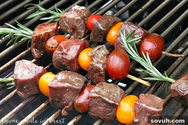 Rosemary Steak Skewers sizzling on a hot grill, showcasing the beautiful sear and char developing on the balsamic-glazed steak and cherry tomatoes, creating an inviting outdoor cooking scene.