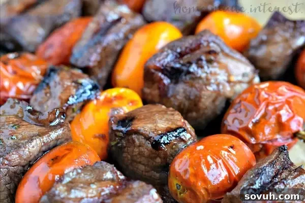 A close-up view of a cooked Balsamic Glazed Rosemary Steak Skewer, showing the juicy, medium-cooked steak, perfectly charred cherry tomatoes, and the fragrant rosemary stalk, highlighting the delicious result.
