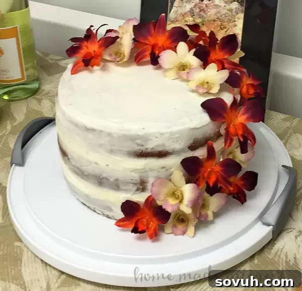 A three-layer coconut mango cake with a 'naked' frosting style, garnished with delicate jasmine flowers, showcasing the tropical elegance.