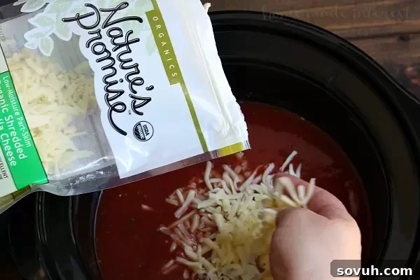 Adding shredded mozzarella cheese to Slow Cooker Pizza Soup for a gooey, melted finish.
