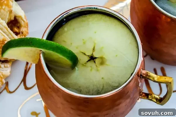 Close-up of a festive Apple Cider Moscow Mule, garnished with apple slices and a lime wedge. The perfect autumn drink for gatherings and celebrations.