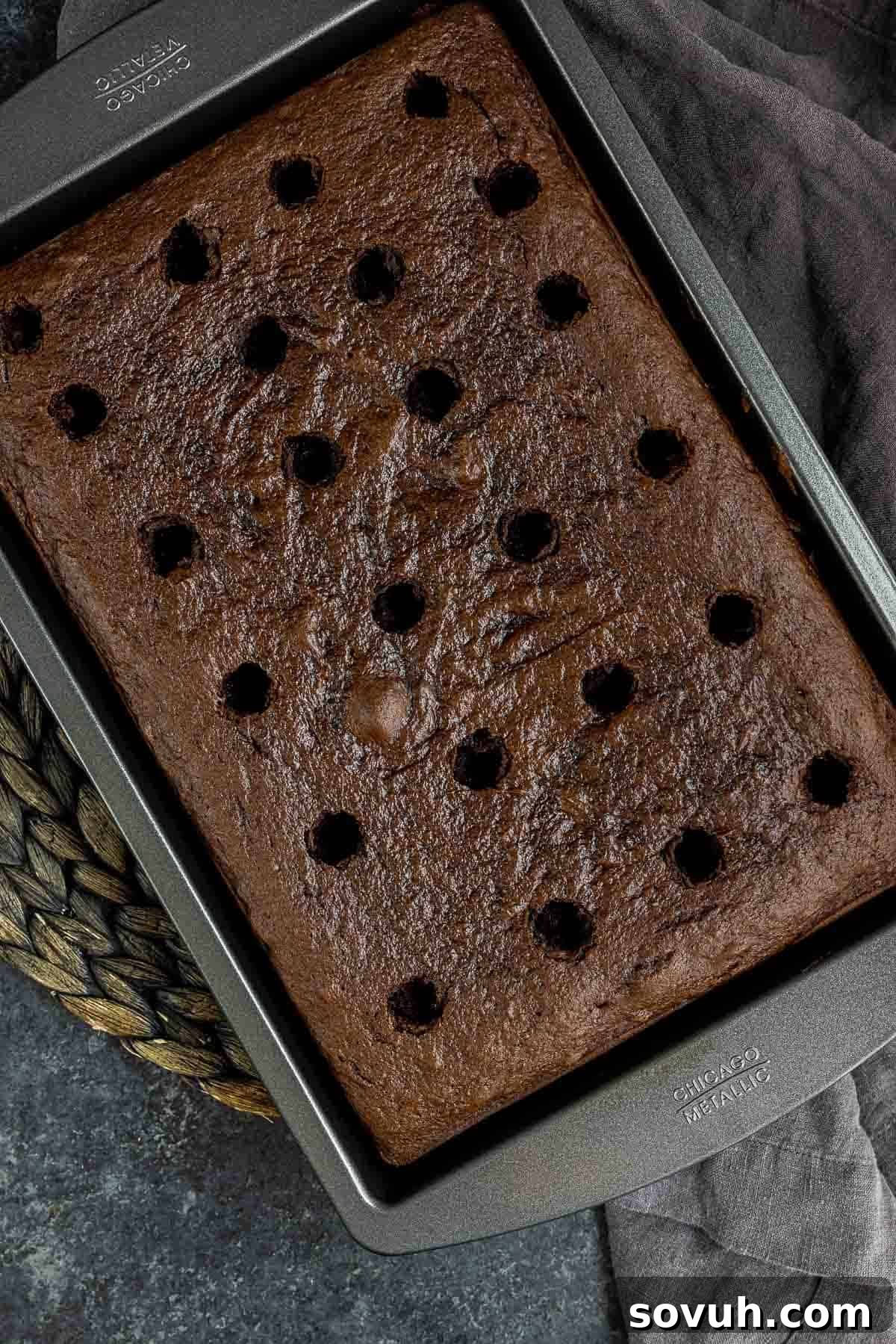 Freshly baked Chocolate Turtle Cake with holes poked across the surface, ready for caramel infusion.