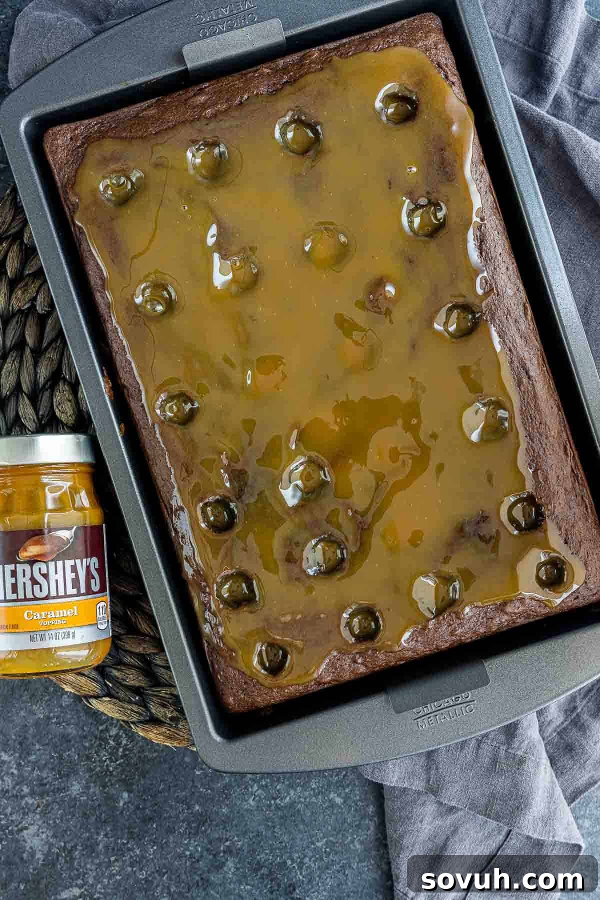 Caramel sauce being poured over the poked Chocolate Turtle Cake, filling each crevice with sweet goodness.