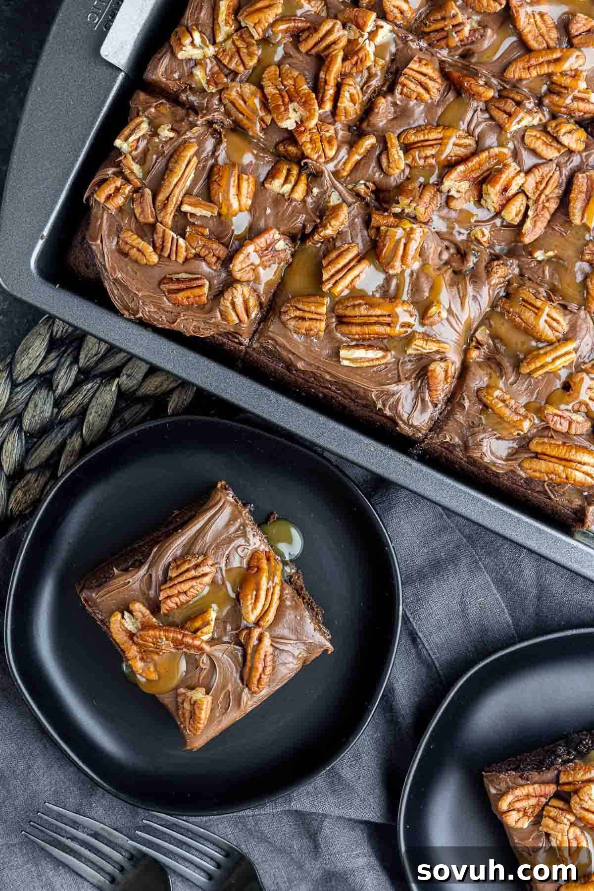 A slice of Chocolate Turtle Cake presented on a black plate next to the full cake in a pan, highlighting its delicious layers.