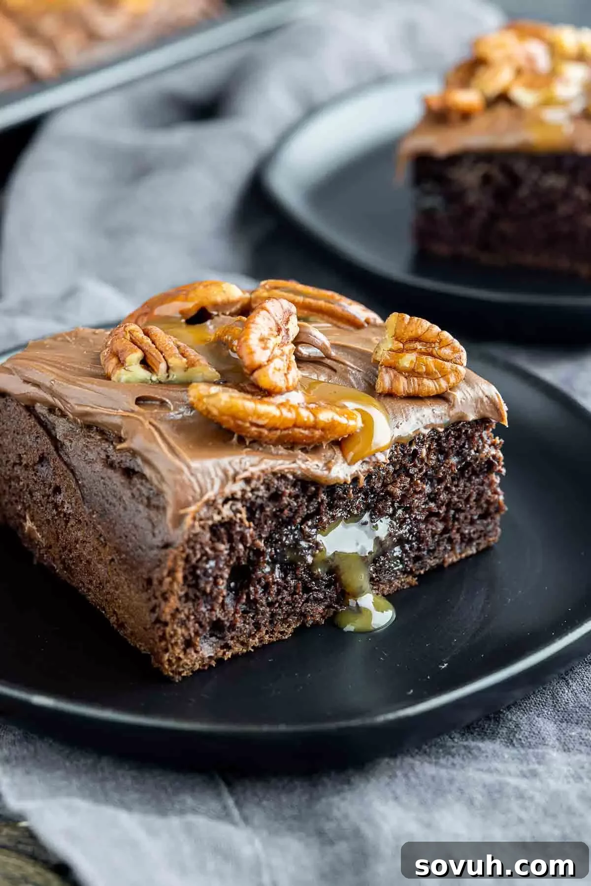 Close-up of a slice of Chocolate Turtle Cake on a black plate, showing the moist chocolate cake, rich caramel, and pecan topping.