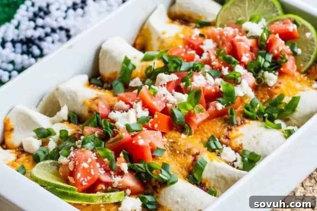 A tray of tender beef enchiladas, generously topped with diced tomatoes, vibrant green onions, melted cheese, and fresh lime slices, ready to serve.