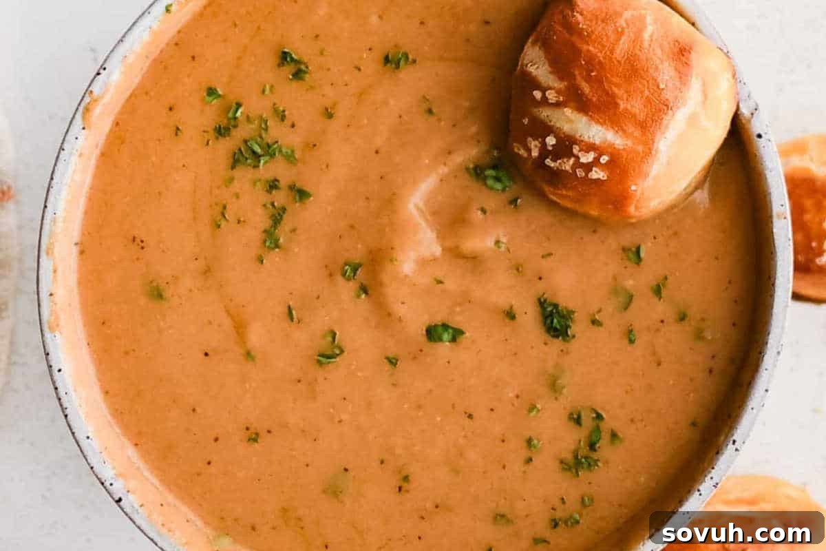 A creamy, pub-style Beer Cheese dip served in a rustic bowl, garnished with fresh herbs, ready for dipping with soft pretzel bites, evoking warmth and flavor.
