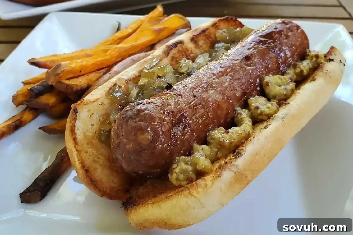 Juicy Beer-Boiled Brats, perfectly grilled and nestled in a toasted bun with generous dollops of mustard and relish, served alongside sweet potato fries on a white plate.
