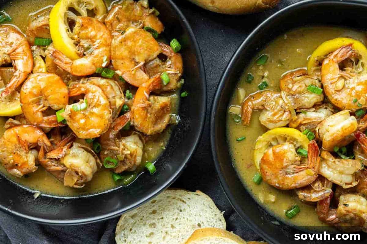 Two dark bowls showcasing succulent New Orleans BBQ shrimp bathed in a rich, creamy, and tangy butter sauce, garnished with fresh lemon slices and vibrant green onions, with crusty bread for dipping.