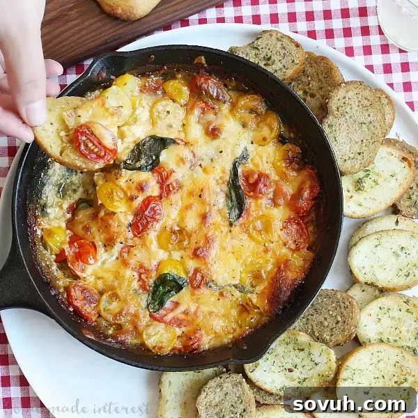 Close-up of the Baked Caprese Dip, fresh out of the oven, showing melted, bubbly mozzarella cheese, vibrant red tomatoes, and green basil leaves.