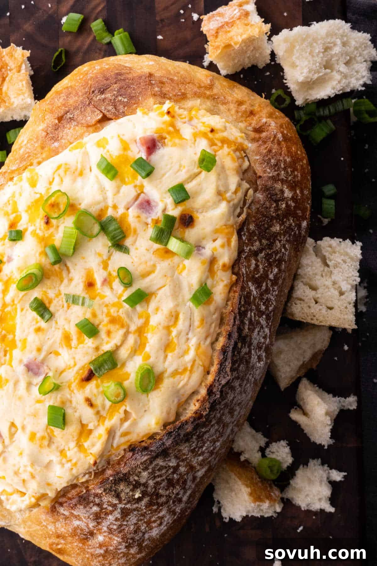 Bread bowl filled with creamy cheese dip, topped with chopped green onions, surrounded by torn bread pieces.