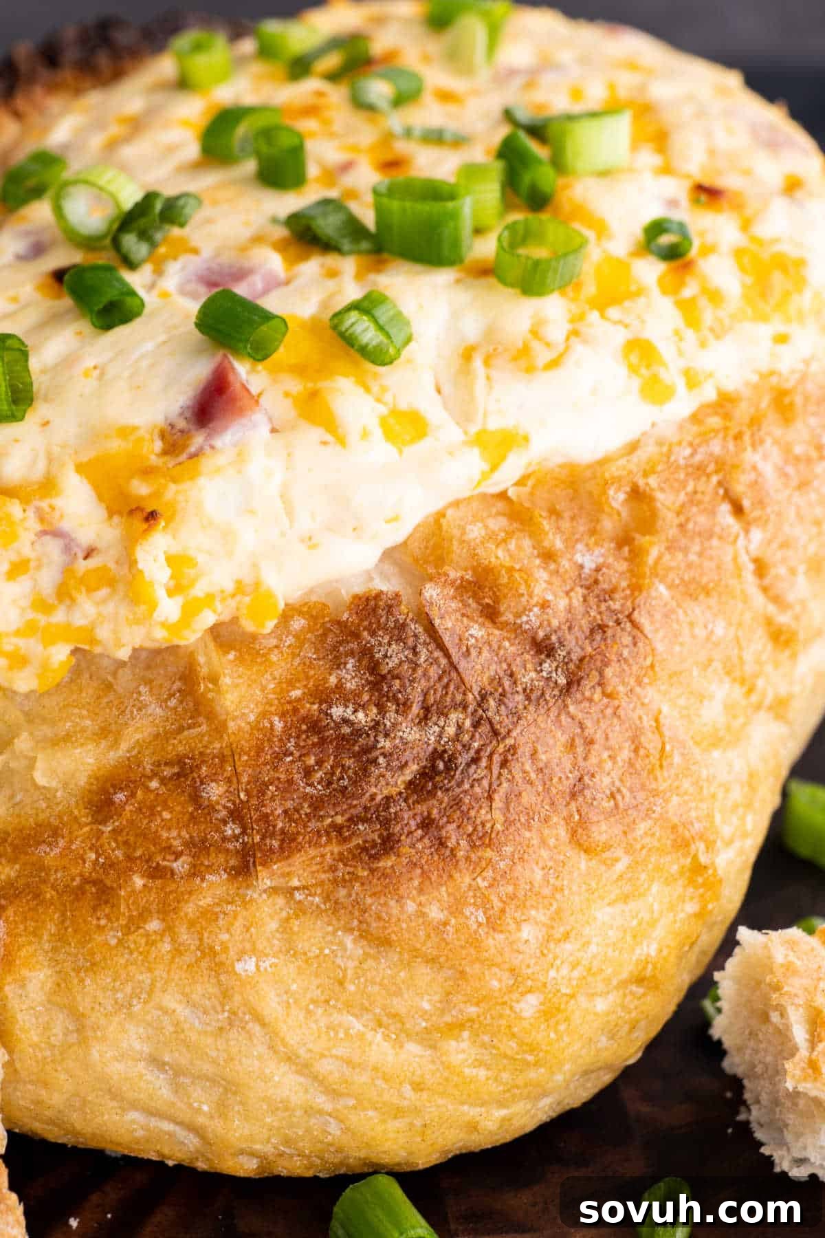 Close-up of a hollowed-out bread loaf filled with melted cheese, topped with chopped green onions.