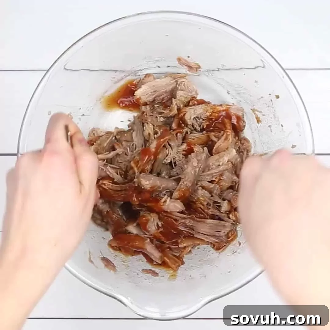 Shredded Instant Pot Pulled Pork in a clear glass bowl, glistening with BBQ sauce and ready to be served.