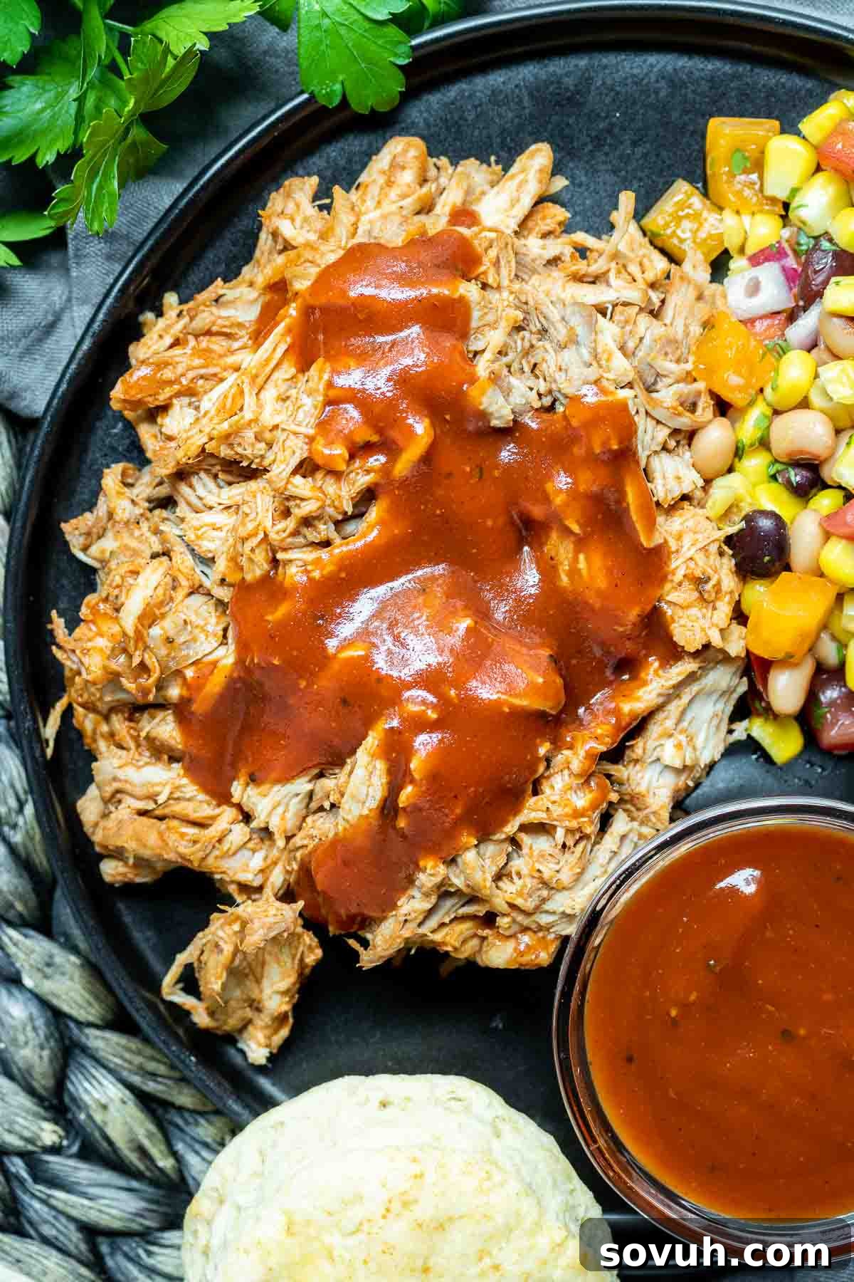 Delicious Instant Pot Pulled Pork served on a white plate with a warm biscuit and a small bowl of extra BBQ sauce on the side.