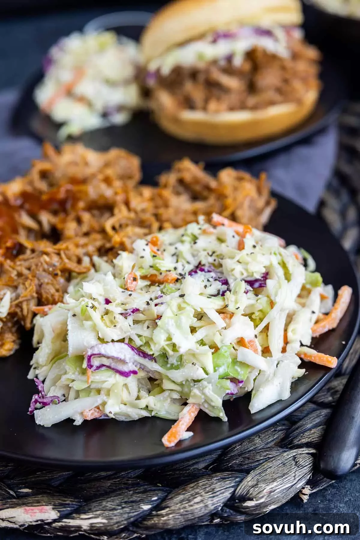 A bowl of creamy, traditional Southern Coleslaw on a black plate, a perfect refreshing accompaniment to rich BBQ pulled pork.