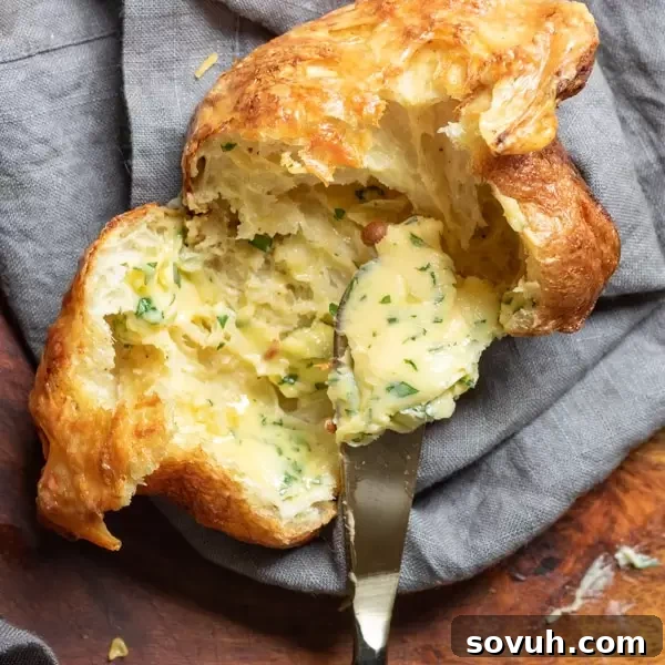 Spreading butter on freshly baked Gruyere Popovers, highlighting their golden crust and fluffy texture.