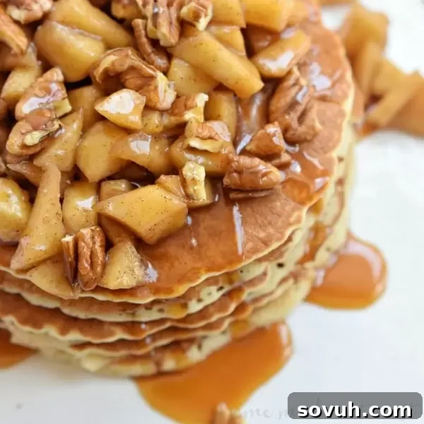 A stack of golden Caramel Apple Pecan Pancakes generously topped with baked apples, chopped pecans, and a rich caramel sauce, ready to be enjoyed as a perfect fall breakfast.