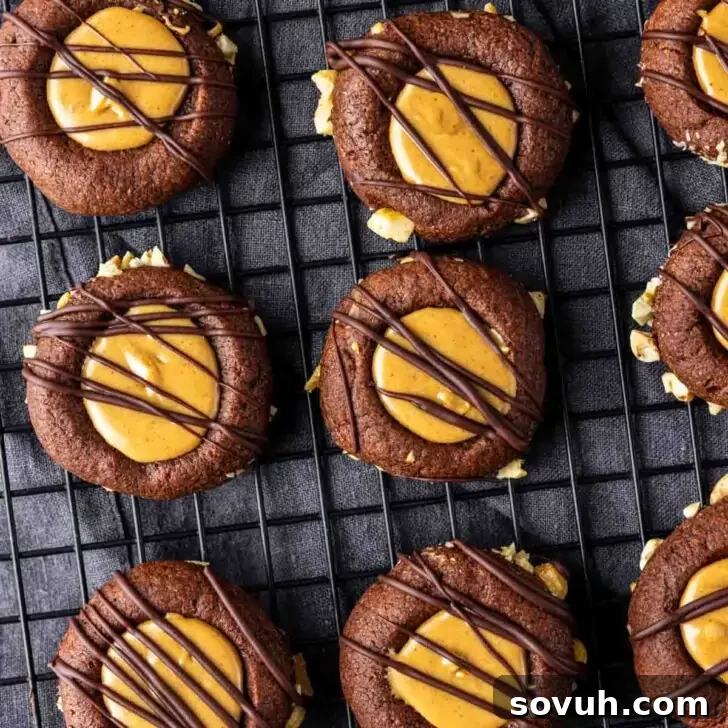 Chocolate thumbprint cookies with peanut butter centers and chocolate drizzle on a cooling rack.