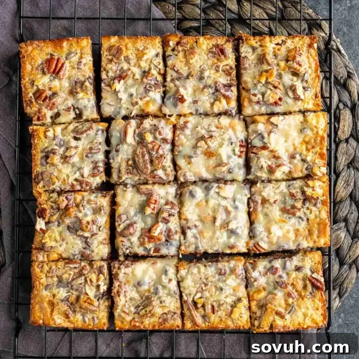 Fifteen square pieces of baked dessert with nuts and melted cheese on a black cooling rack.