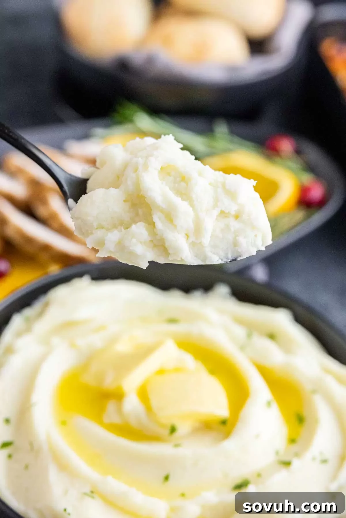 A serving spoon lifting a spoonful of the creamy Not Your Mom's Mashed Potatoes from a bowl.