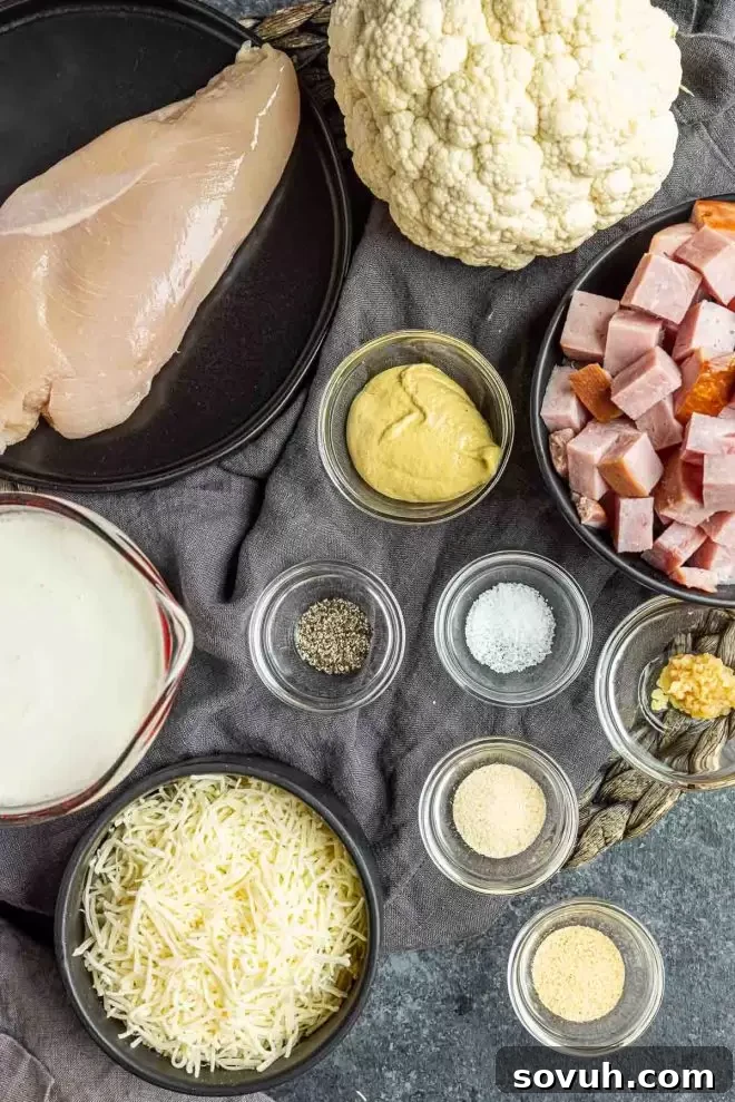A selection of fresh ingredients laid out for making Keto Chicken Cordon Bleu Casserole, including cauliflower, chicken, ham, various cheeses, and spices