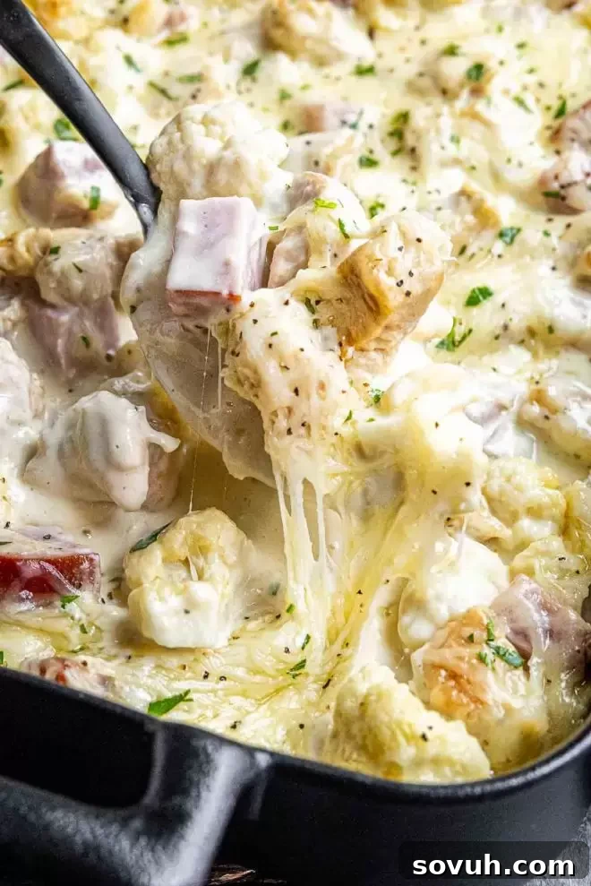 A scoop of Keto Chicken Cordon Bleu Casserole being lifted from the dish, showcasing the layers of cauliflower, chicken, ham, and melted cheese