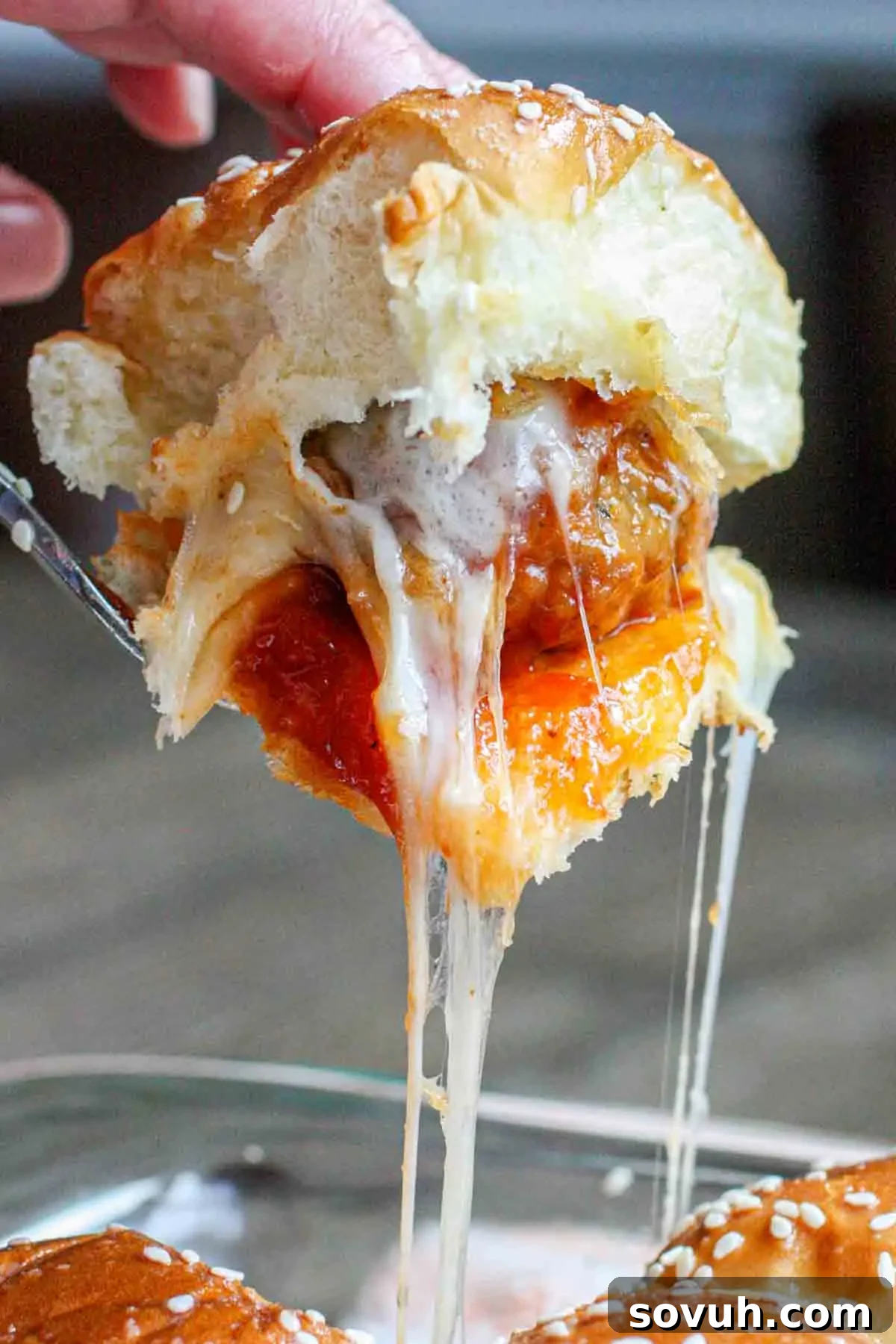 Effortless Tangy Meatball Sliders 4 A hand holding a meatball slider with melted cheese, tomato sauce, and sesame seed bun.